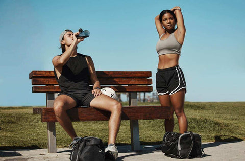 Two young athletes resting and hydrating outdoors after workout session focusing on recovery phase supplements