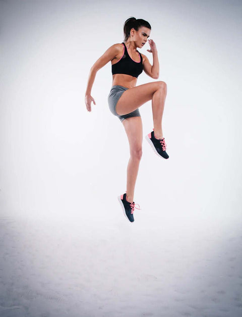 Athletic woman in workout clothes performing a high knee exercise for post-training nutrition and recovery.