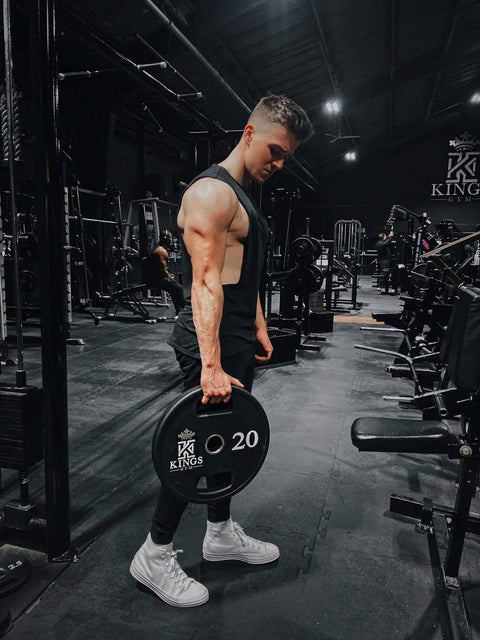 Muscular man holding a 20 kg weight plate in a gym illustrating sports nutrition and performance related to Ernährungspsychologie.