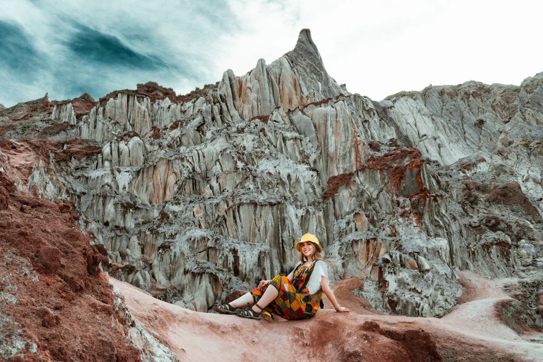 Woman sitting on rocky terrain with dramatic cliffs and cloudy sky, illustrating salt and hydration concept in sports performance.